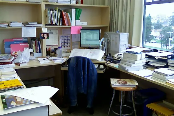 Desk cluttered with books, files and a screen